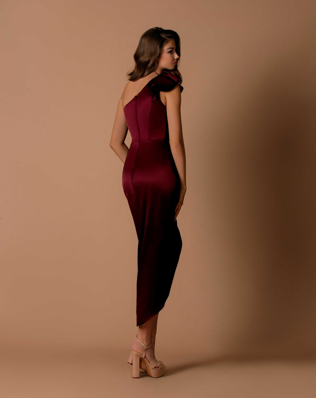 Woman wearing a burgundy one-shoulder dress against a brown background