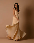 Woman in a flowing beige dress against a brown background