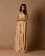 Woman wearing a long beige dress against a brown background
