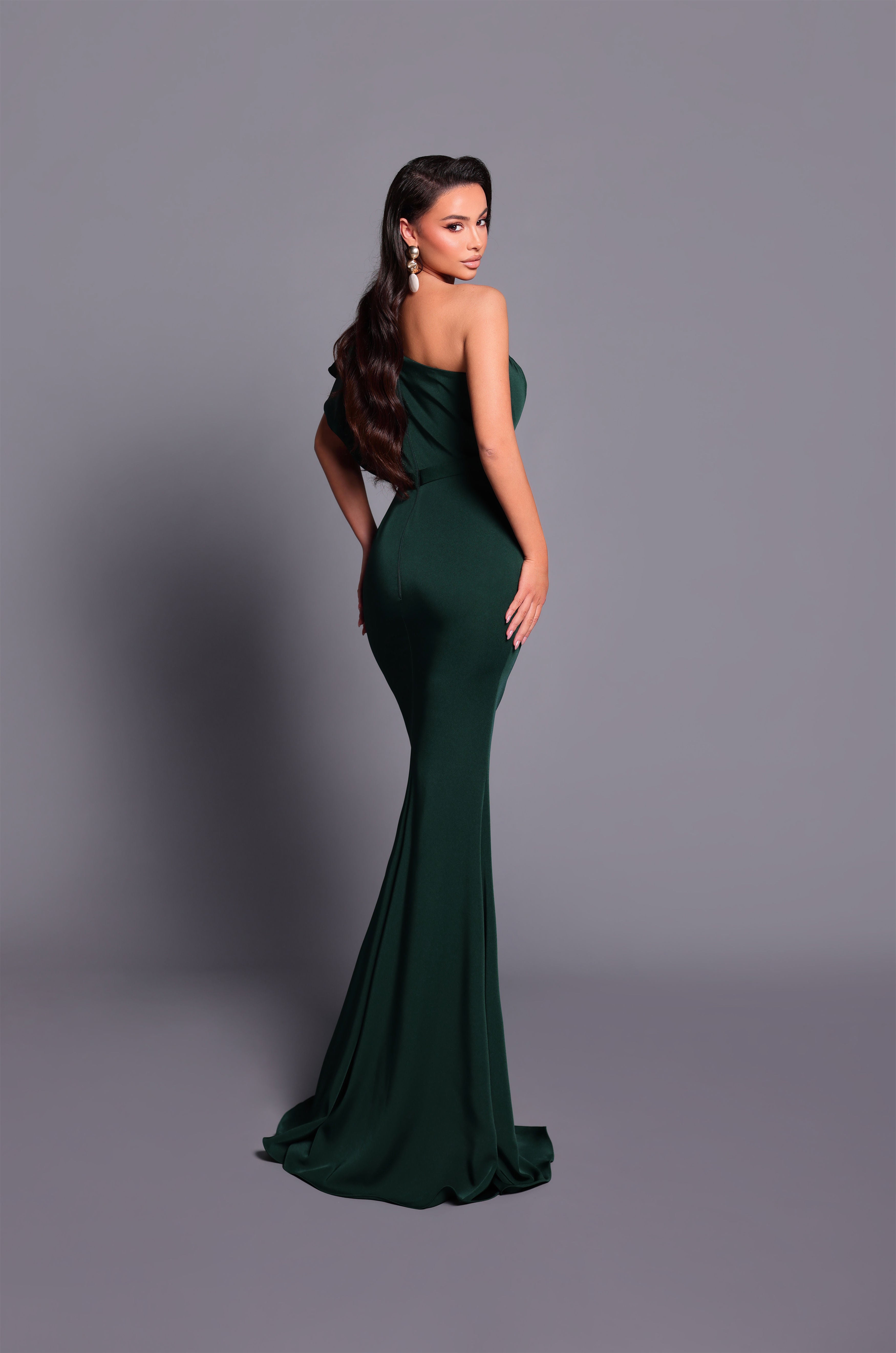 Woman wearing a dark green strapless gown against a gray background