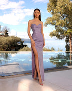 Woman in a strapless purple gown with a high slit standing by a pool with trees and sky in the background