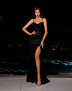 Woman in a black evening gown with a high slit standing on a rooftop at night.