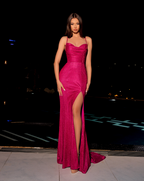 Woman in a pink evening gown with a high slit standing outdoors at night.