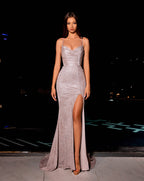 Woman in a silver evening gown with a high slit standing on a dark background