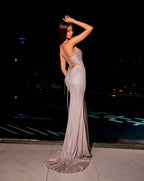 Woman in a silver evening gown posing by a pool at night.