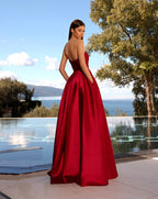 Woman in a red evening gown standing by a pool with a scenic background