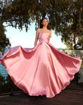 Woman in a pink strapless gown standing outdoors with trees and water in the background
