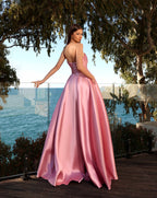Woman in a pink evening gown standing outdoors with trees and water in the background