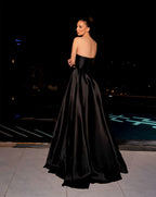 Woman in a black strapless gown standing on a dark background