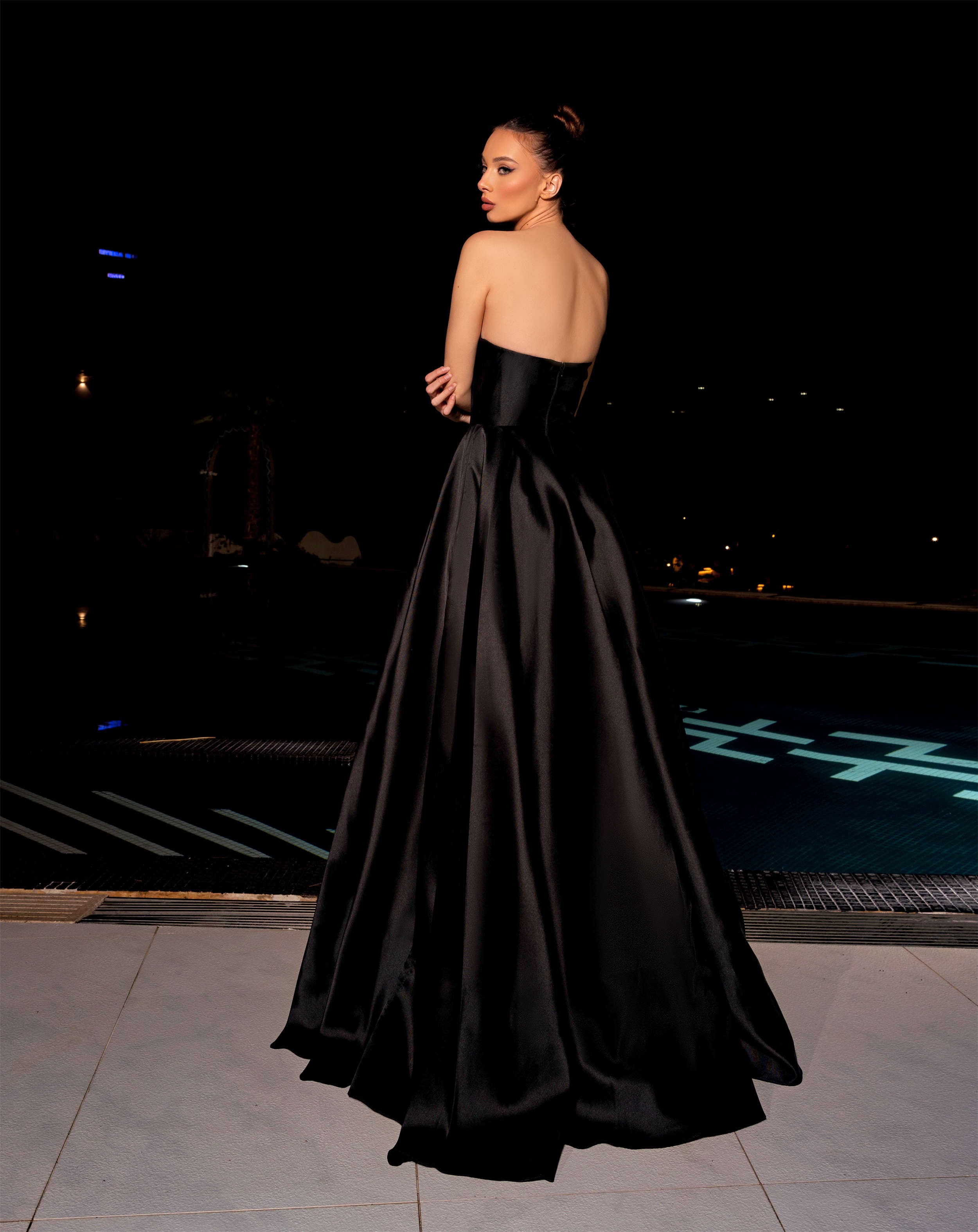 Woman in a black strapless gown standing on a dark background