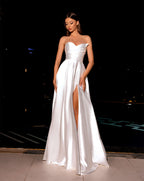 Woman wearing a white strapless gown with a high slit on a dark background