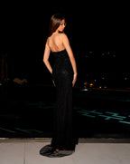 Woman in a black strapless gown standing by a pool at night.