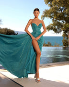 Woman in a teal strapless gown with a high slit standing by a pool with ocean view.