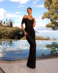 Woman in a black evening gown standing by a pool with a scenic background