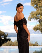 Woman in a black evening gown standing outdoors with trees and sky in the background