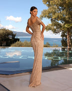 Woman in a beige evening gown standing by a pool with a scenic background