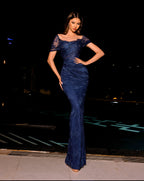 Woman in a blue lace dress standing on a street at night.