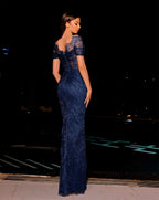 Woman wearing a navy blue lace evening gown against a dark background