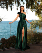 Woman in a green evening gown standing by a scenic waterfront.