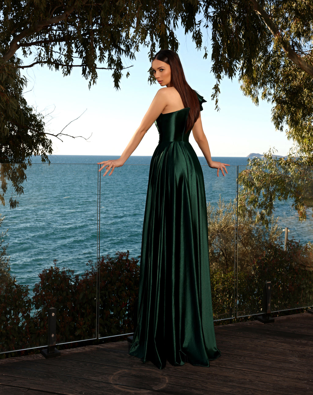 Woman in a green dress standing by a body of water with trees in the background