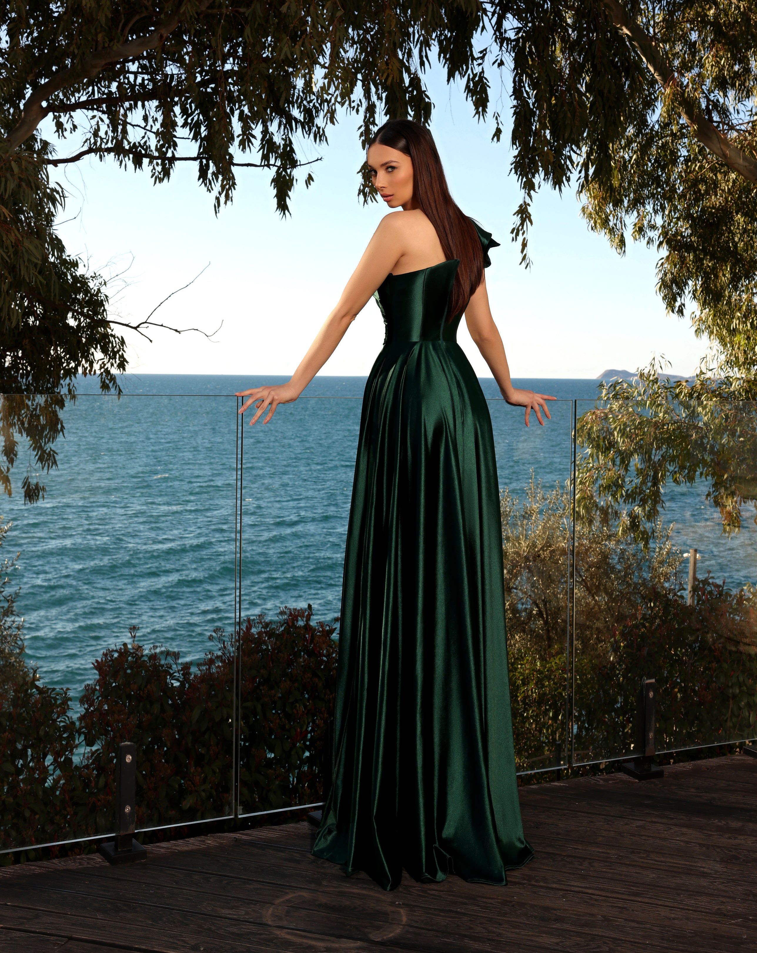 Woman in a green dress standing by a body of water with trees in the background