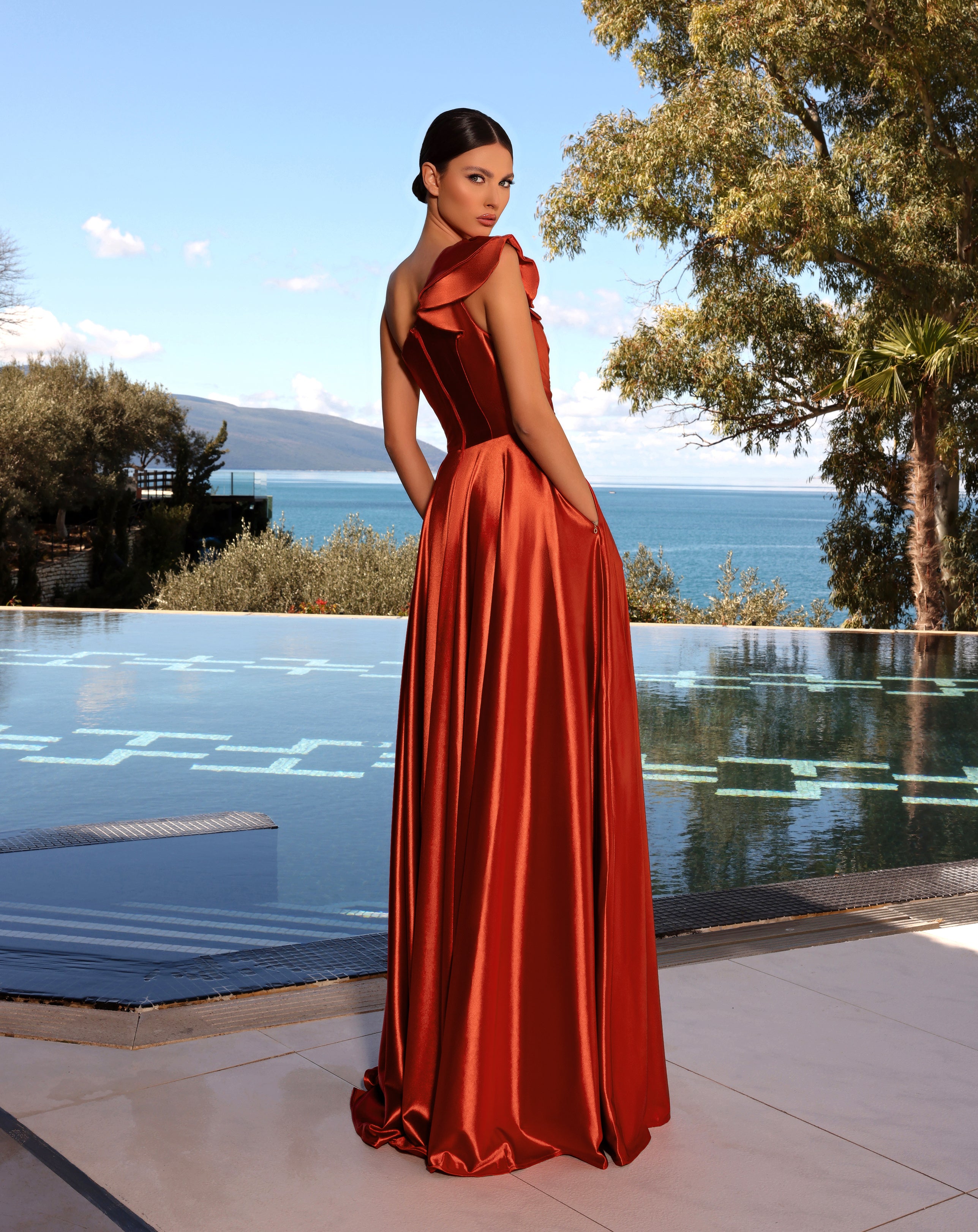 Woman in a red evening gown standing by a pool with a scenic background