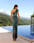 Woman in a green one-shoulder dress standing by a pool with a scenic view.