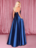 Woman in a blue satin gown standing against a pink curtain backdrop