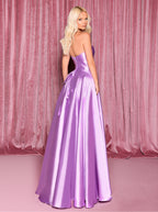Woman wearing a purple strapless gown against a pink curtain backdrop