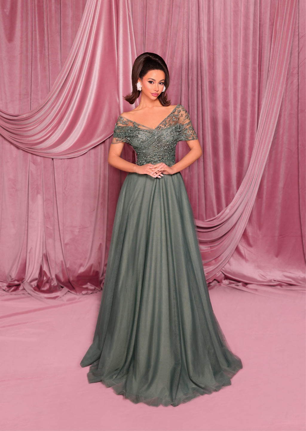 Woman in a green evening gown standing against a pink curtain backdrop