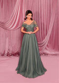 Woman in a green evening gown standing against a pink curtain backdrop