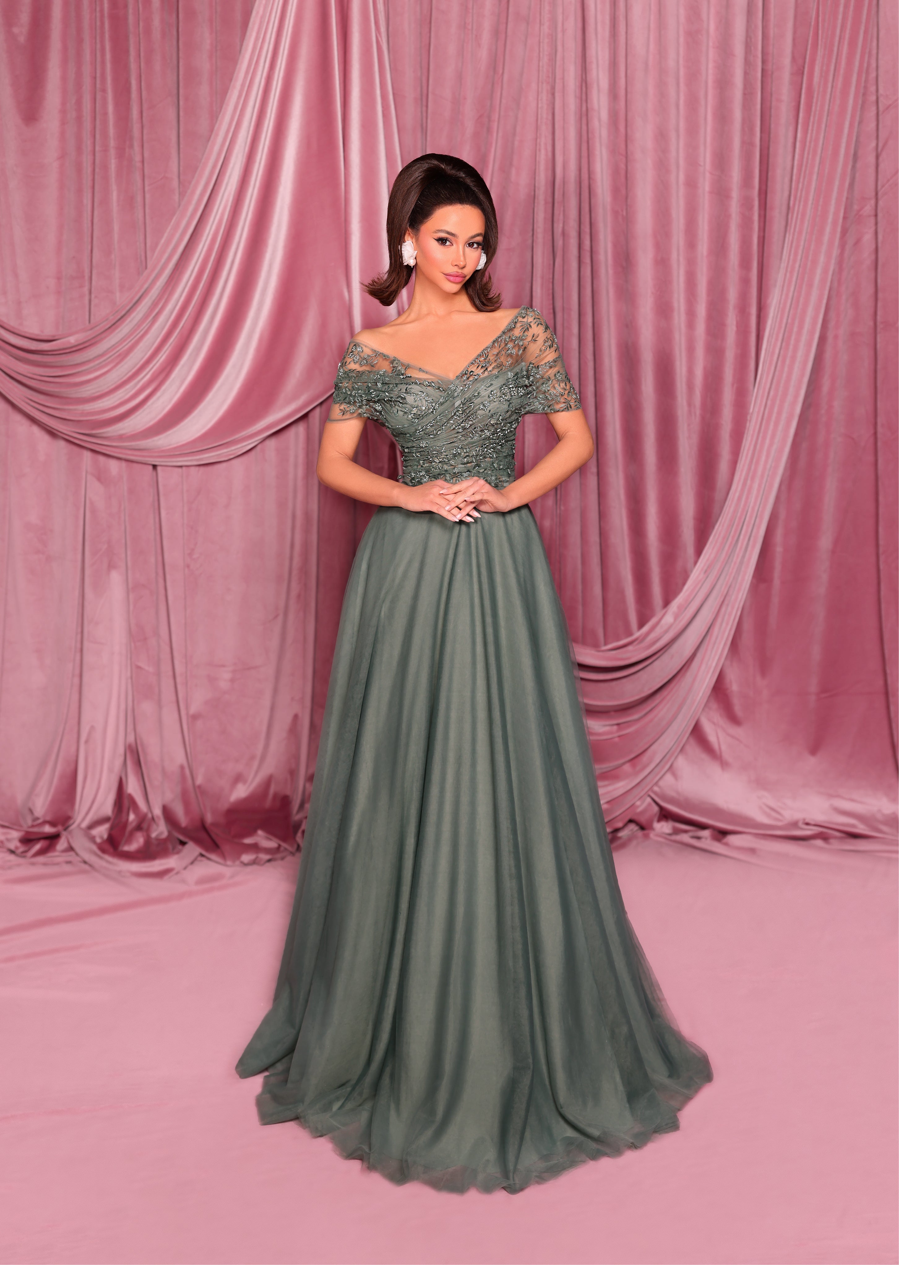 Woman in a green evening gown standing against a pink curtain backdrop