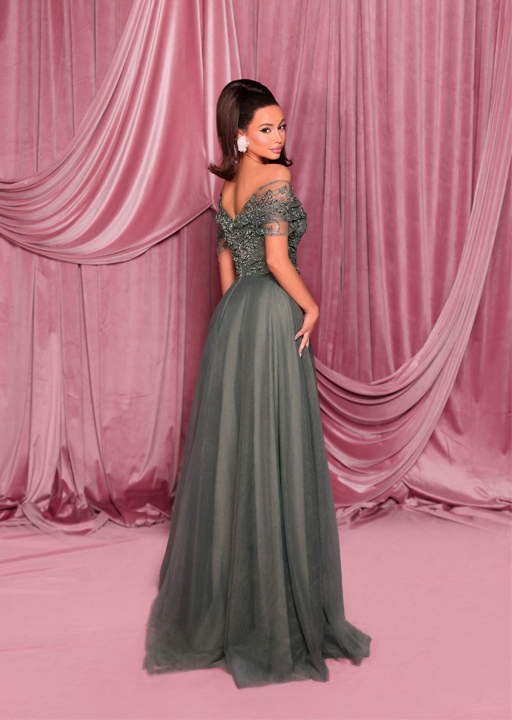 Woman in a green evening gown standing against a pink curtain backdrop
