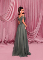 Woman in a green evening gown standing against a pink curtain backdrop