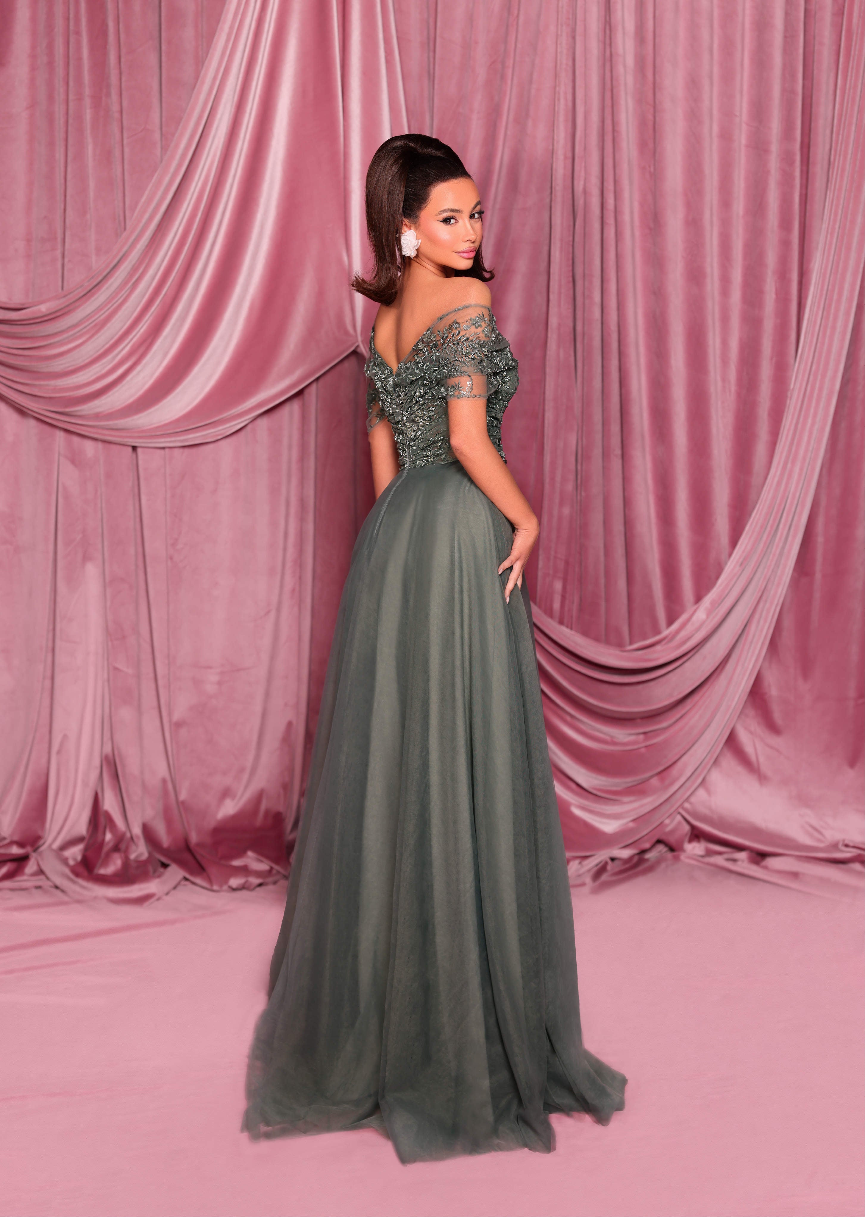 Woman in a green evening gown standing against a pink curtain backdrop