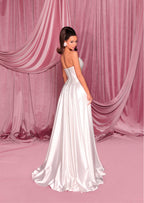 Woman in a white strapless gown standing against a pink draped curtain backdrop