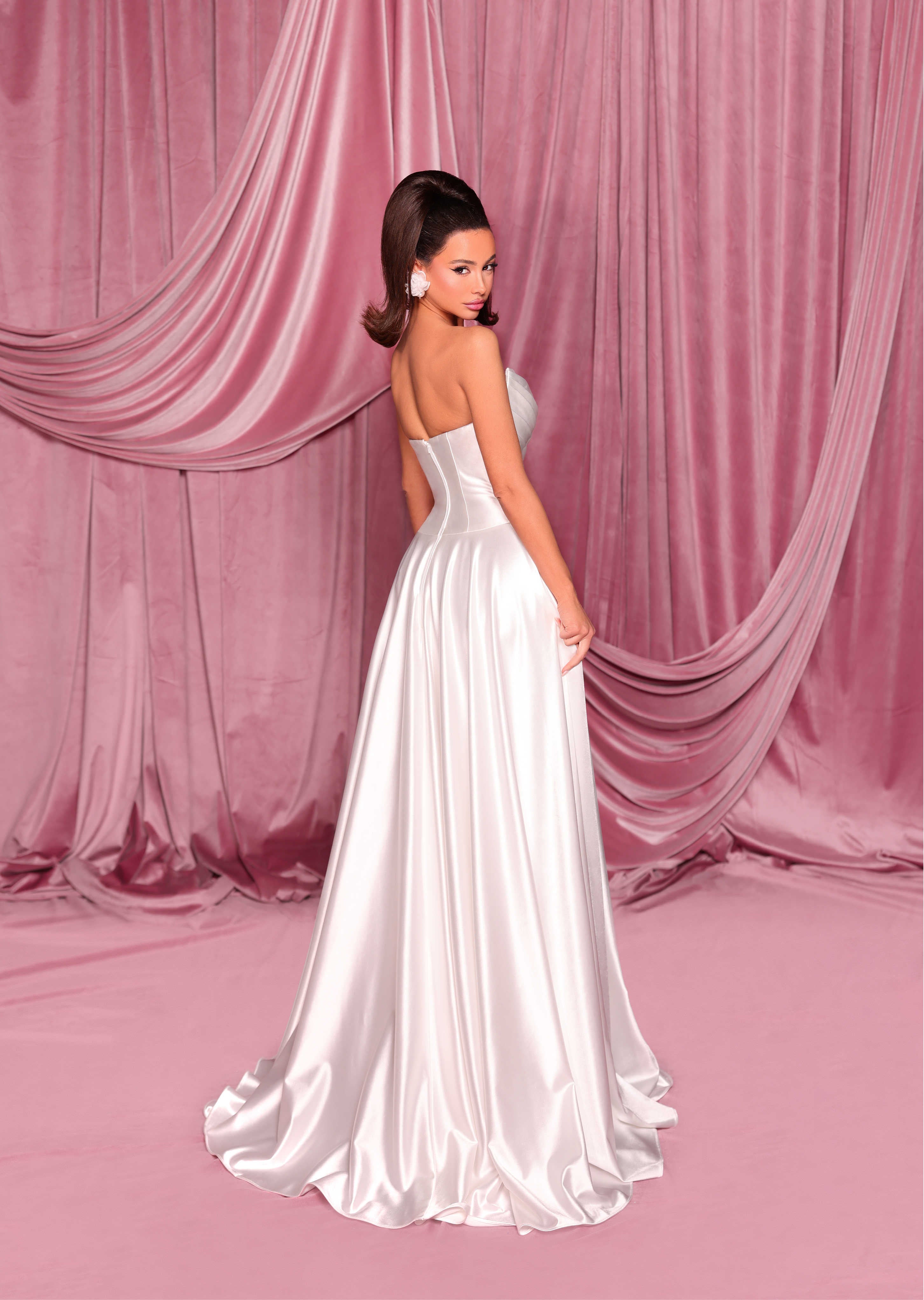 Woman in a white strapless gown standing against a pink draped curtain backdrop