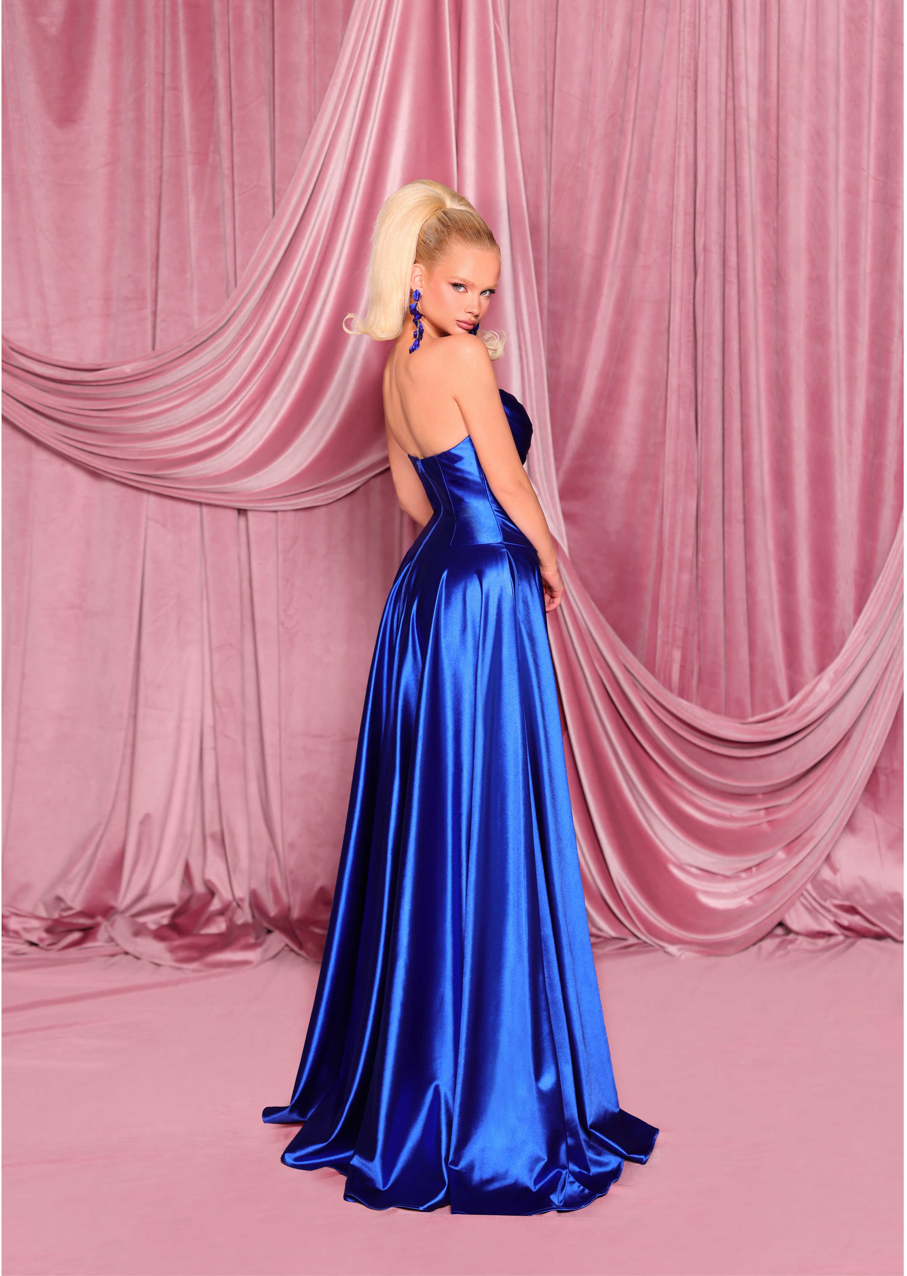 Woman in a blue evening gown against a pink draped curtain backdrop