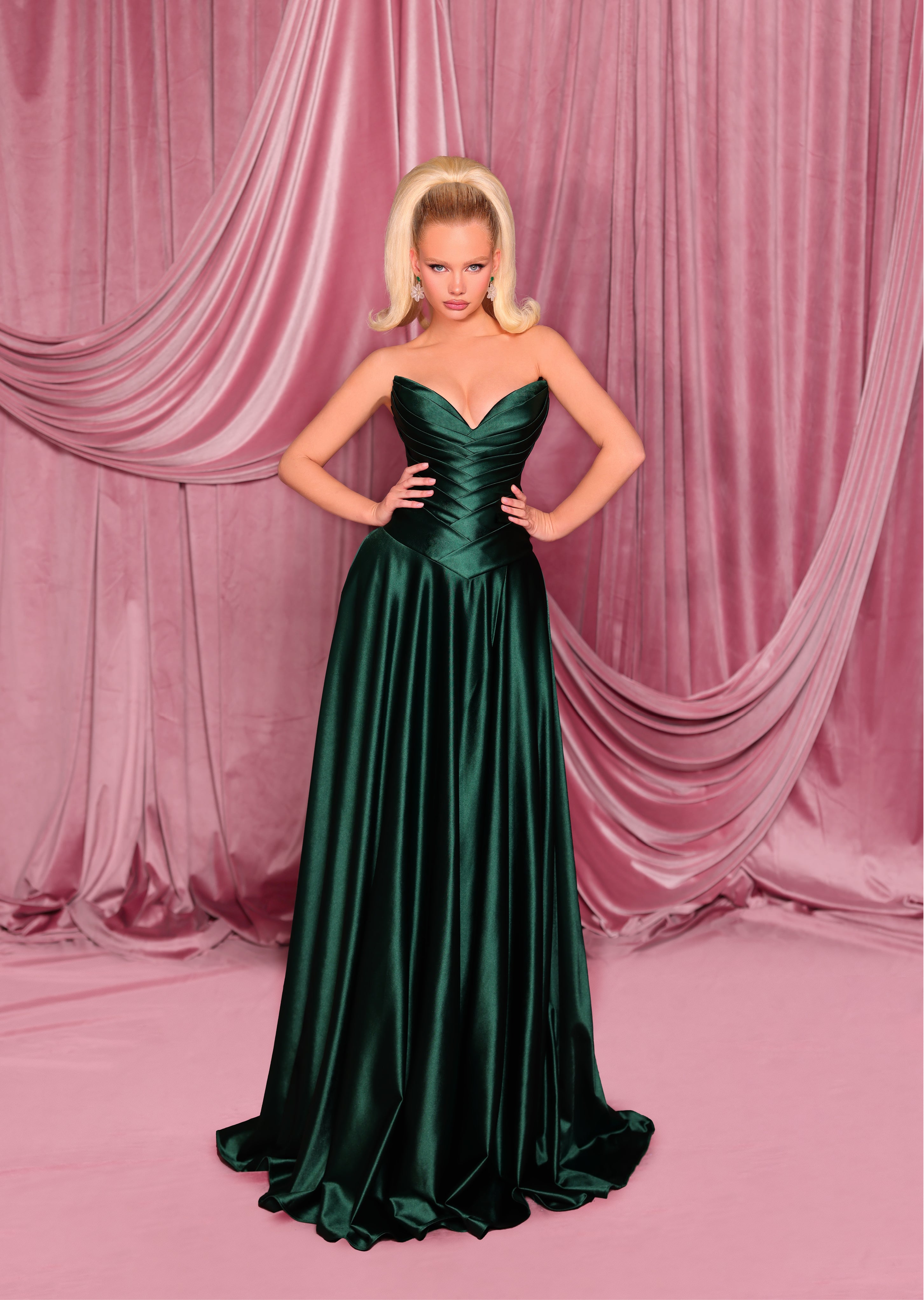 Woman in a green evening gown standing against a pink curtain backdrop