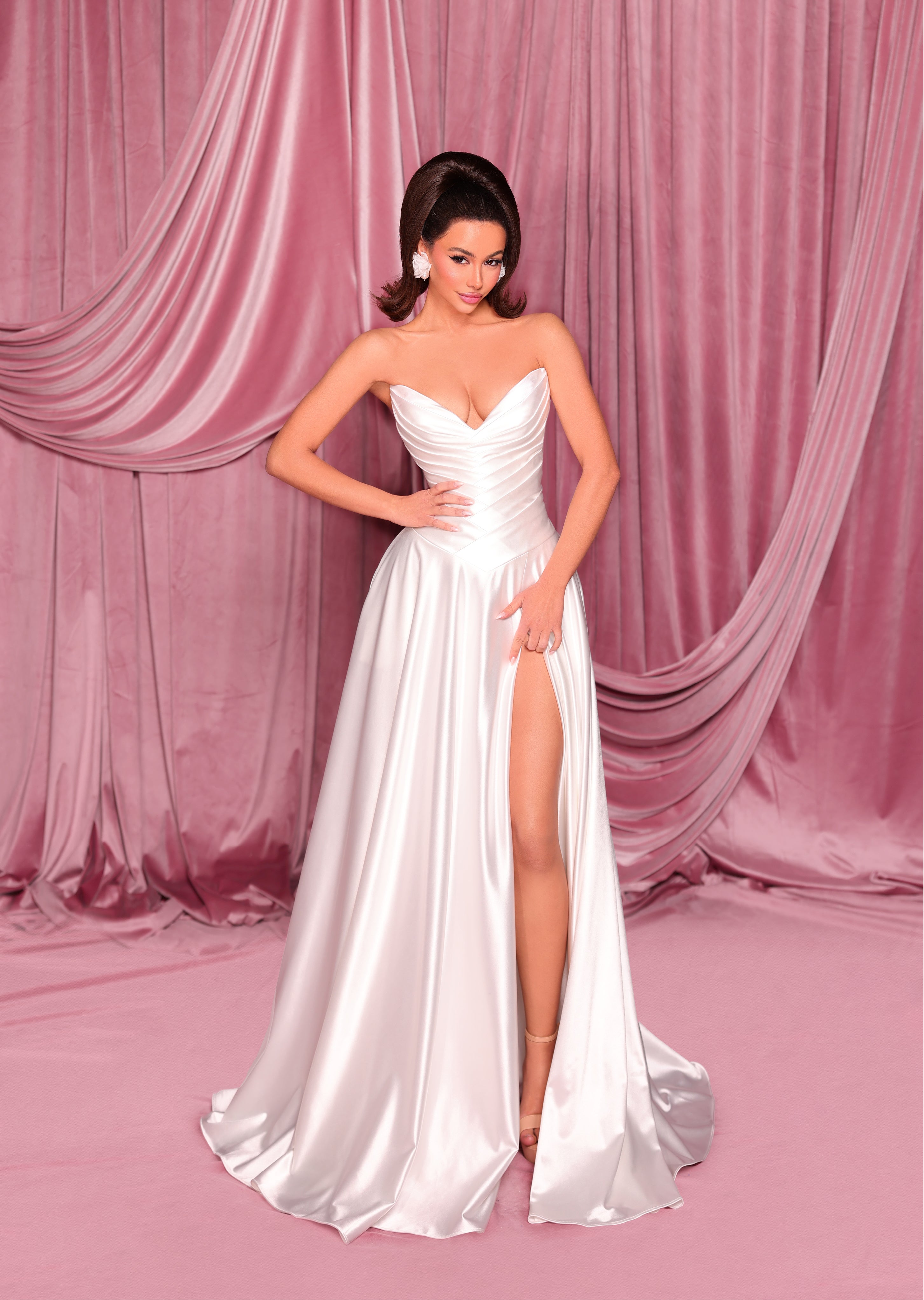 Woman in a white strapless gown with a high slit on a pink draped curtain background