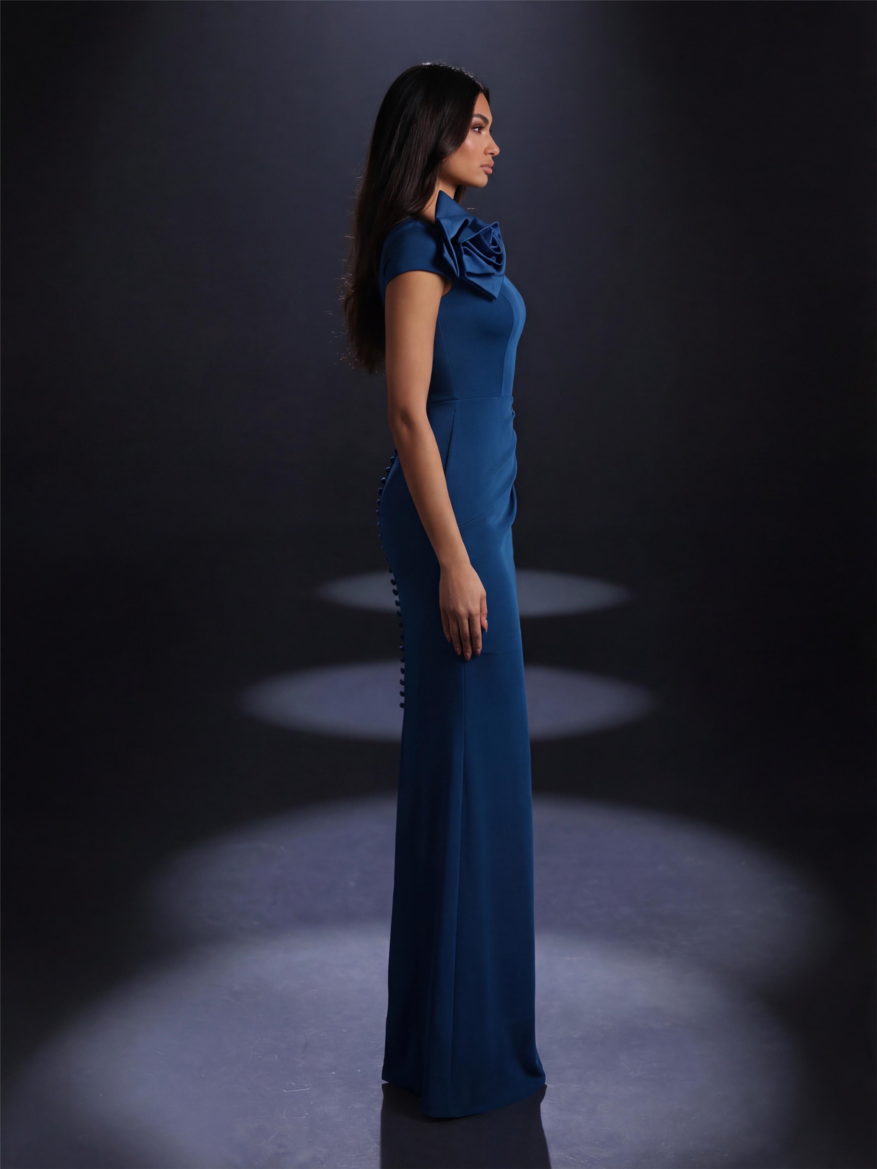 Woman in a blue evening gown standing against a dark background with spotlight effect