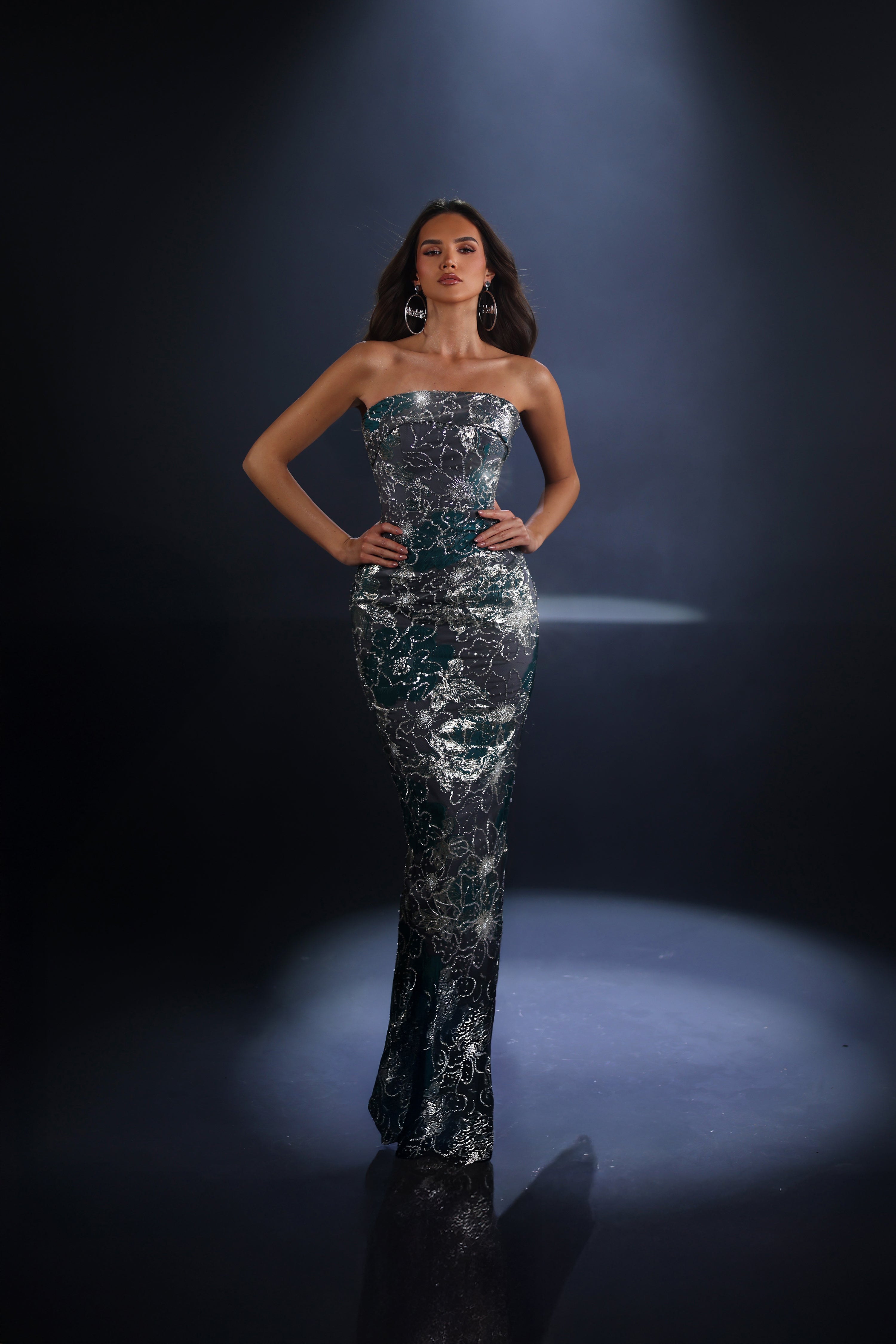 Woman in a sparkling silver dress standing on a dark background with spotlight effect