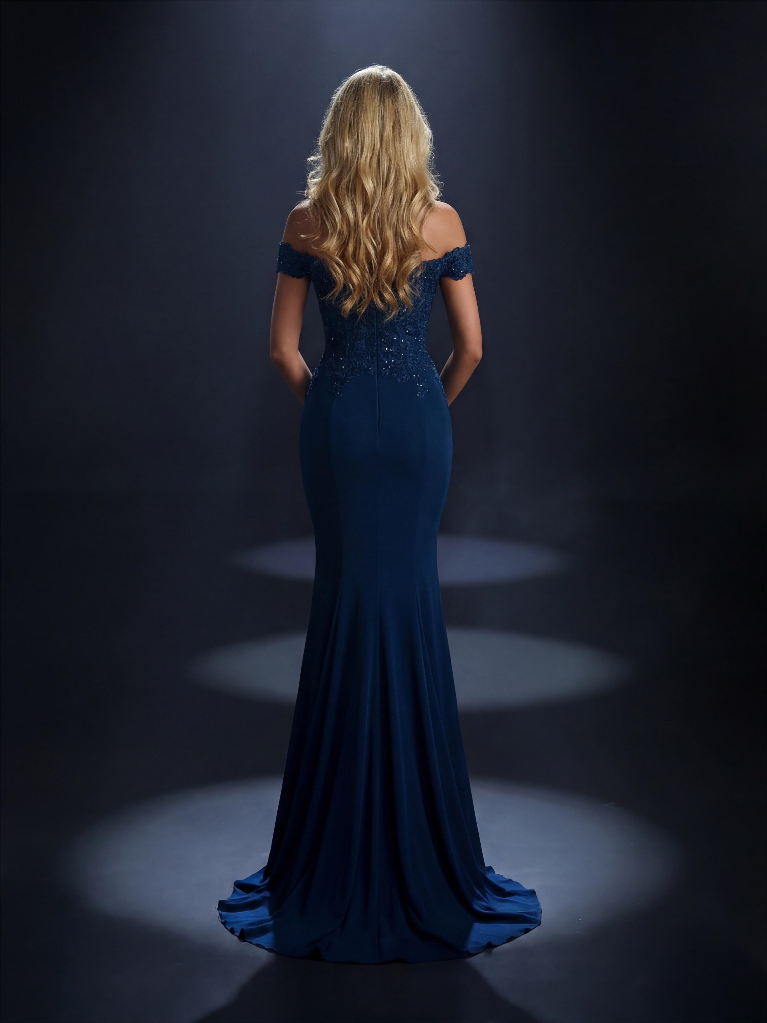 Woman in a blue evening gown standing in a spotlight against a dark background
