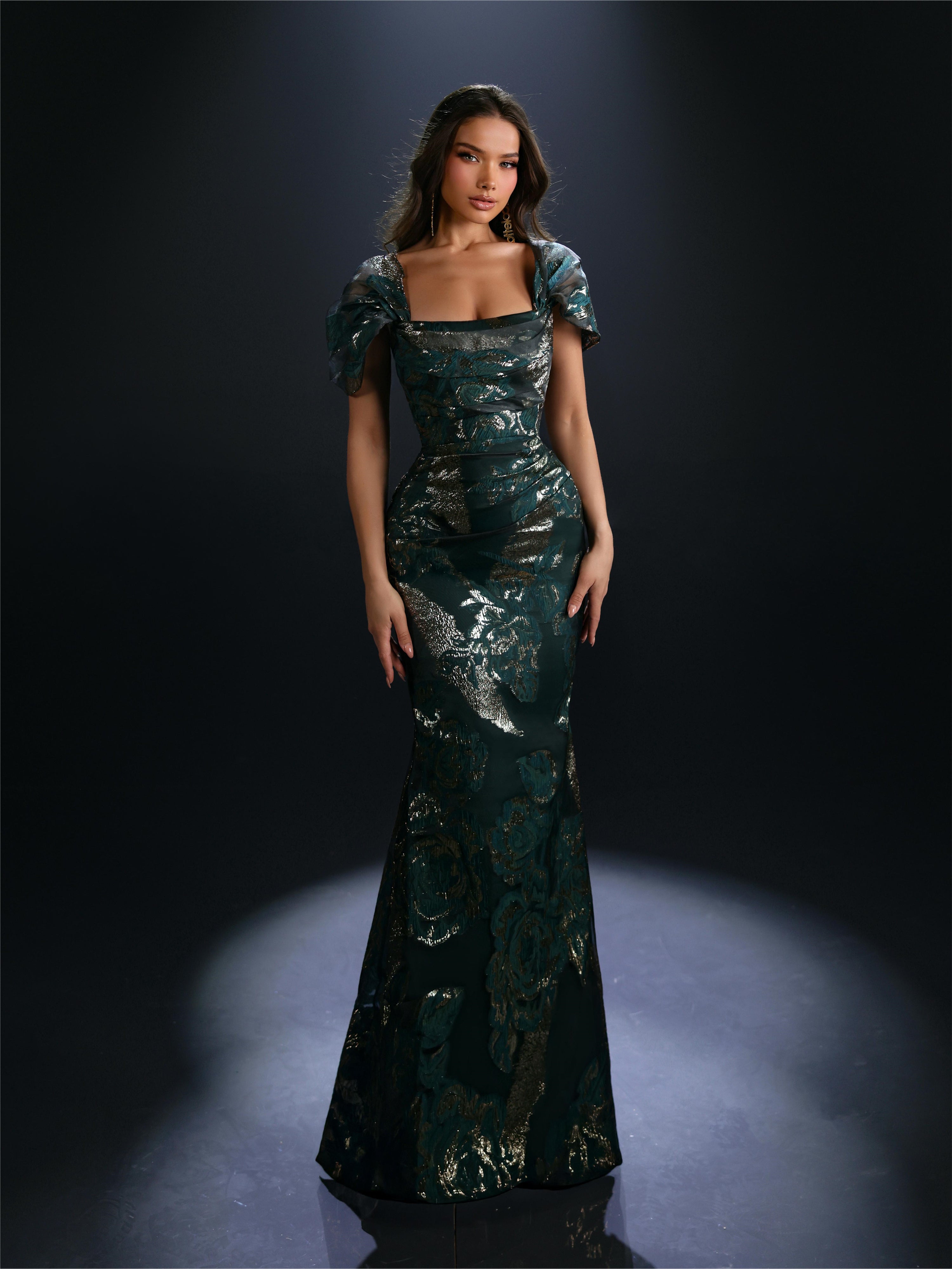 Woman wearing a green evening gown with floral patterns against a dark background