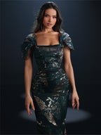 Woman wearing a dark green dress with floral patterns against a black background