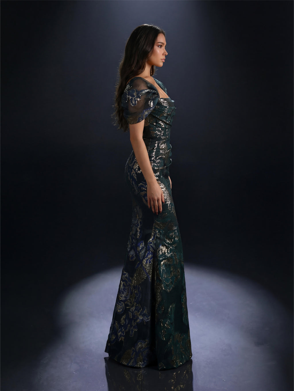 Woman in a dark green sequined evening gown against a black background