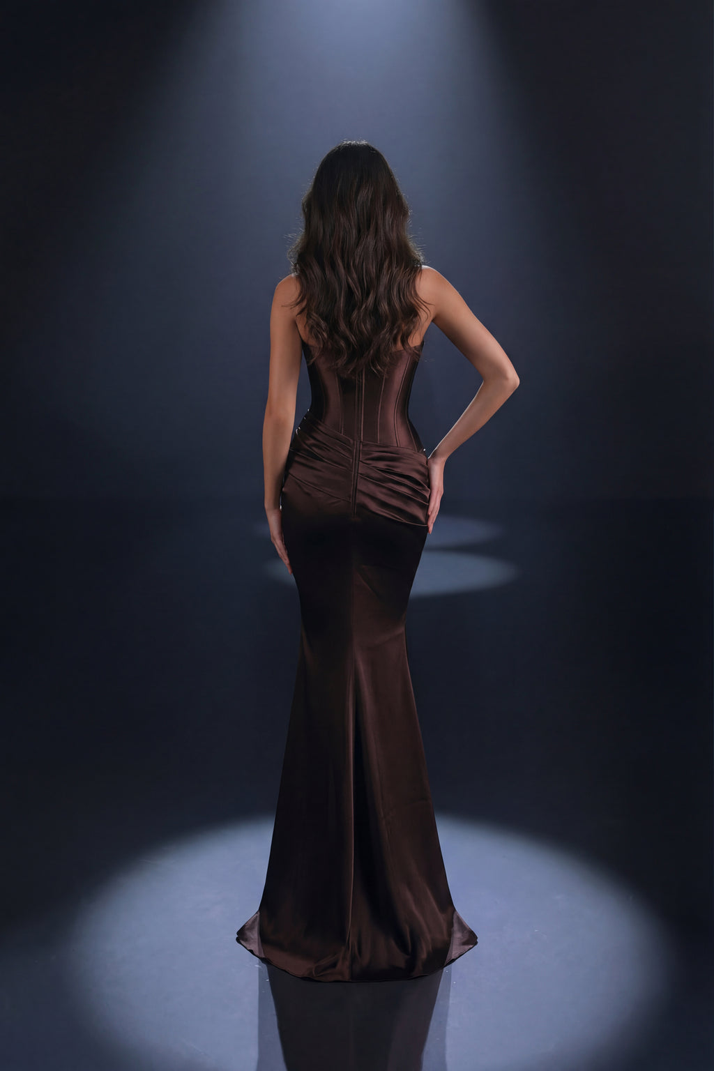 Woman in a brown evening gown standing in spotlight on a dark background