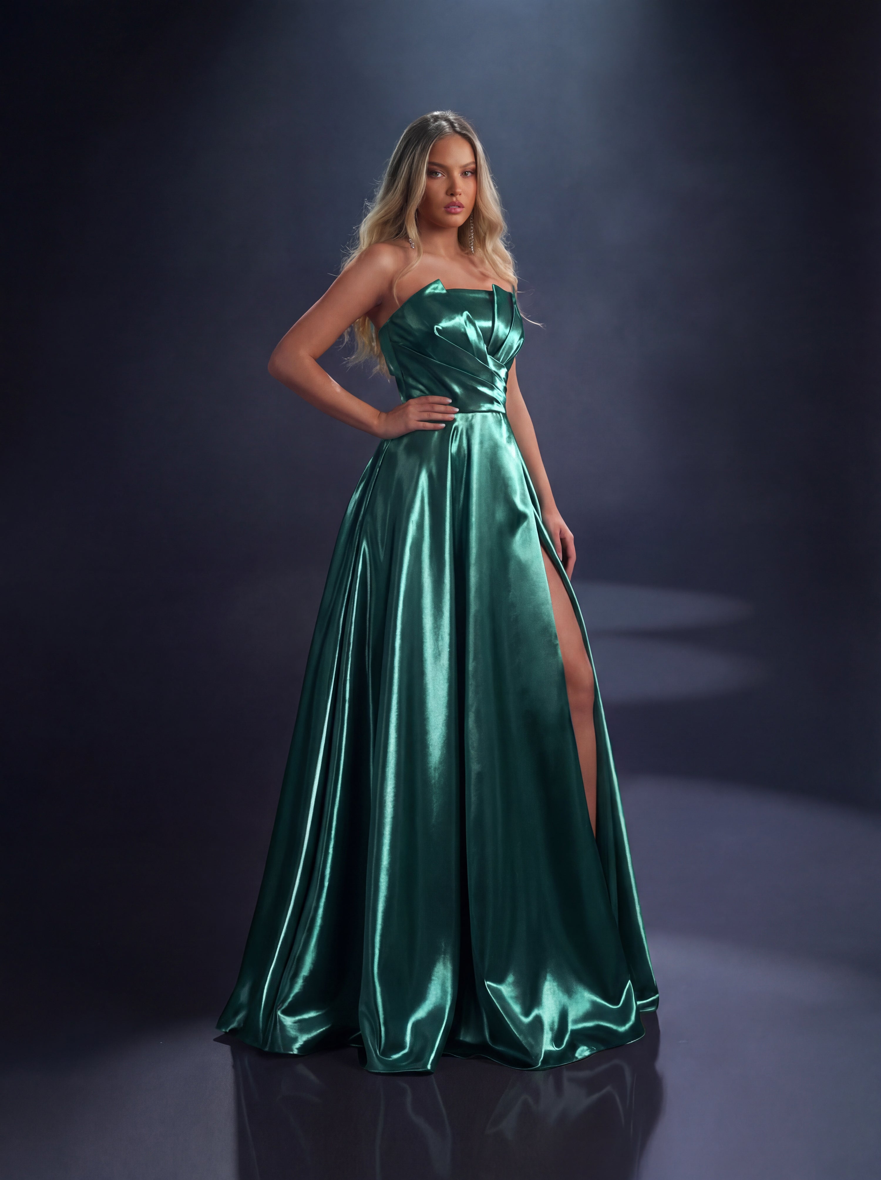Woman wearing a green satin gown with a slit on a dark background