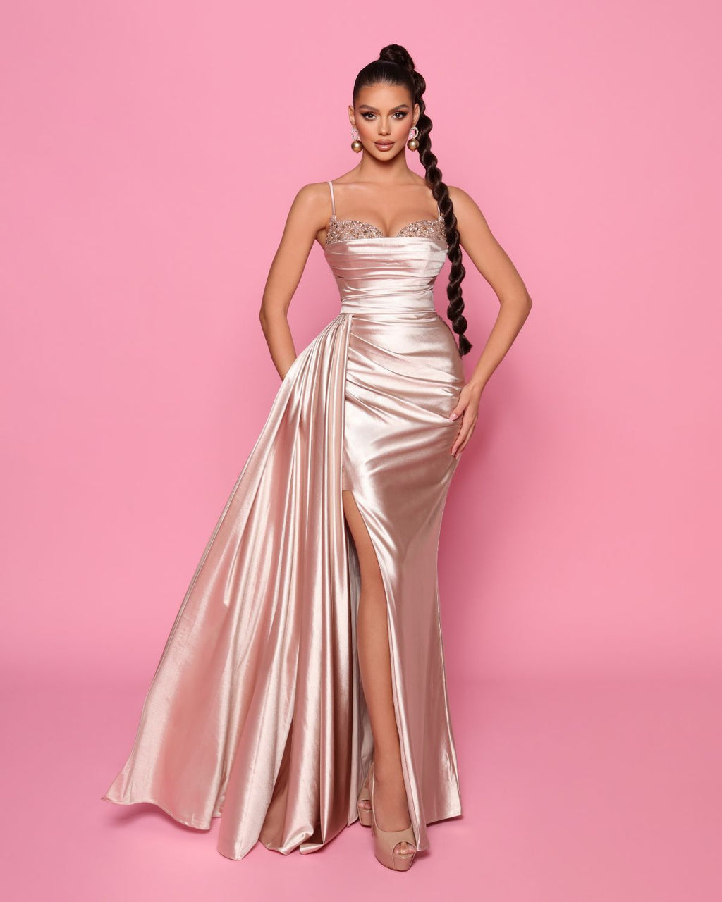 Woman wearing a pink satin evening gown with a high slit on a pink background
