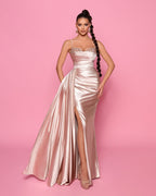 Woman wearing a pink satin evening gown with a high slit on a pink background